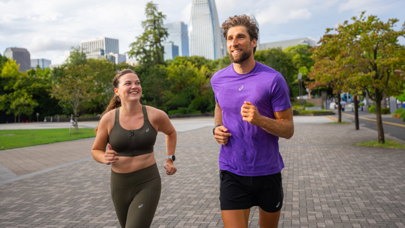 A man and a woman jogging in a park with a skyline in the background.